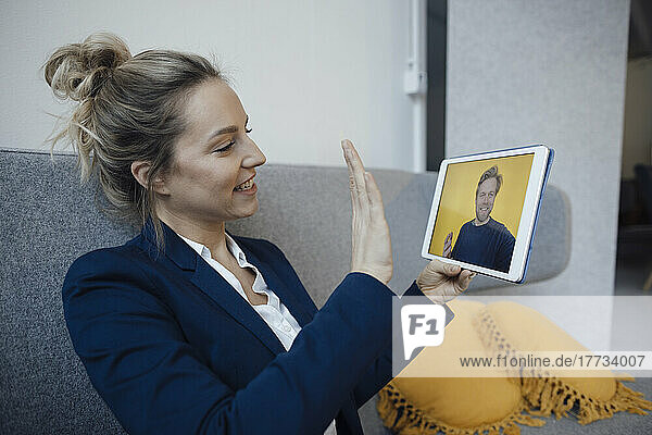 Businesswoman gesturing on video call through tablet PC sitting on sofa in office