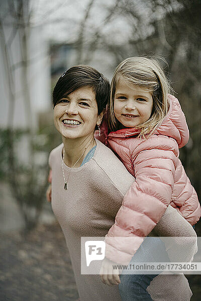 Smiling woman giving piggyback ride to daughter outdoors