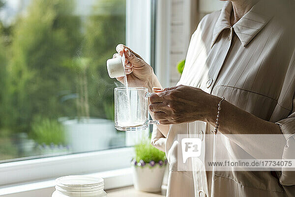 Close-up of woman pouring powder into glass at the window