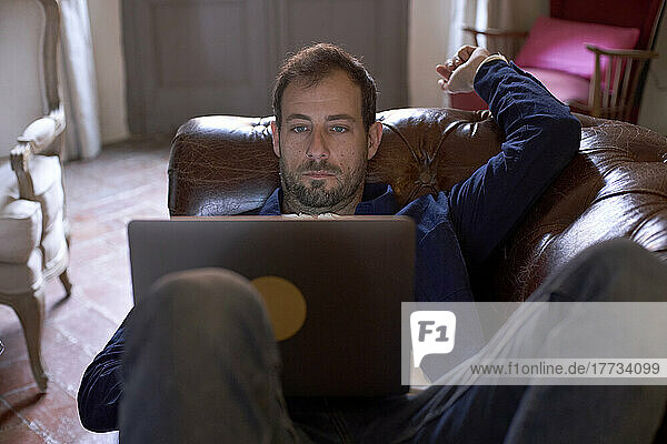 Man lying on couch in living room using laptop