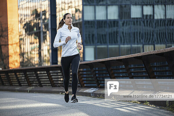 Young woman jogging on footbridge in city