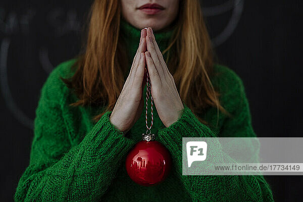 Woman with red Christmas bauble standing against black background