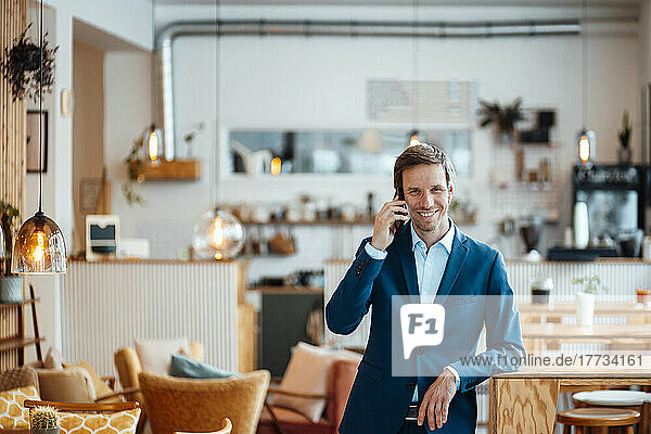 Happy freelancer talking on smart phone at cafe