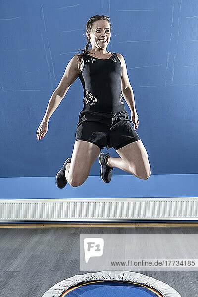 Smiling young woman jumping on small trampoline in fitness room