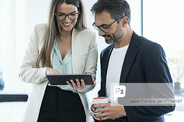 Smiling businesswoman discussing over tablet PC with businessman in office