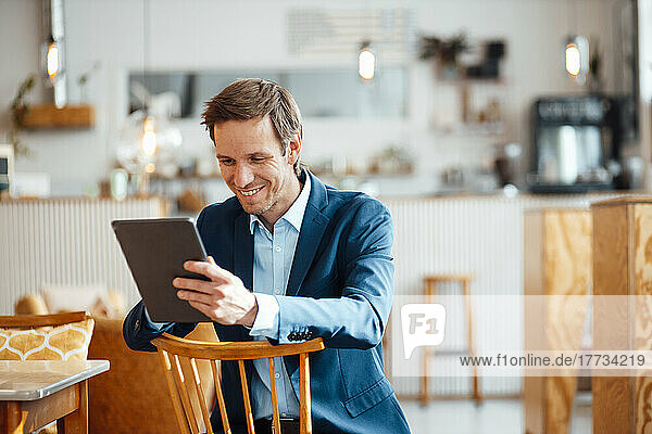 Happy businessman sitting on chair and using tablet PC at cafe