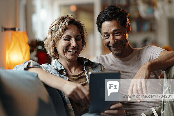Happy couple using tablet PC sitting on sofa at home