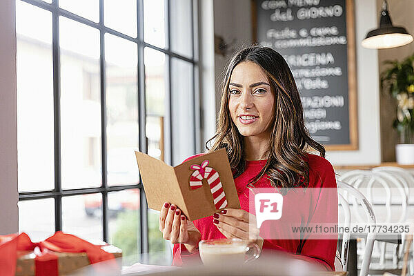 Beautiful young woman with Christmas card sitting in cafe