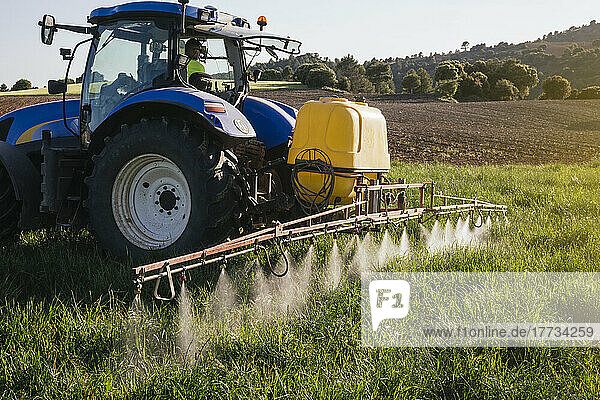 Farmer spraying fertilizer through sprayer sitting in tractor on field