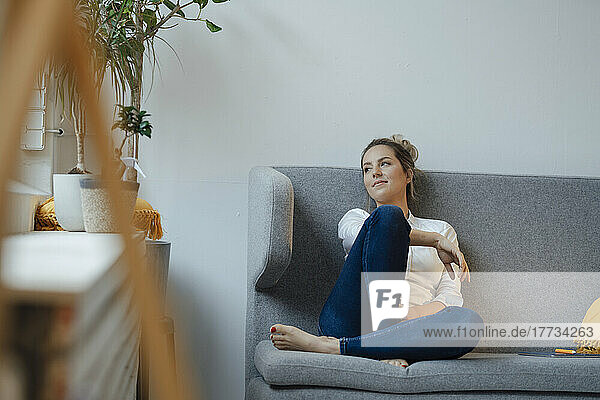 Smiling businesswoman day dreaming on sofa in office