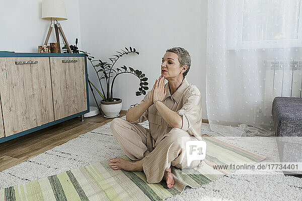 Mature woman with sitting on rug at home meditating
