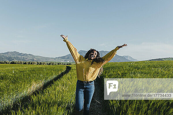 Happy young woman standing with arms raised in meadow