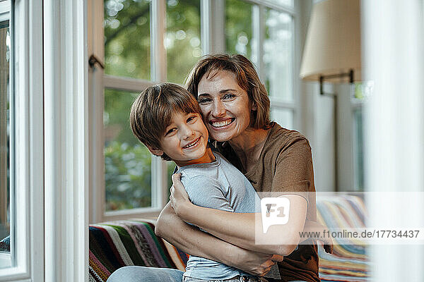 Glückliche Frau umarmt ihren Sohn  der zu Hause auf dem Sofa sitzt