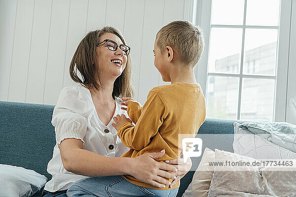 Cheerful mother with son sitting on sofa in living room at home