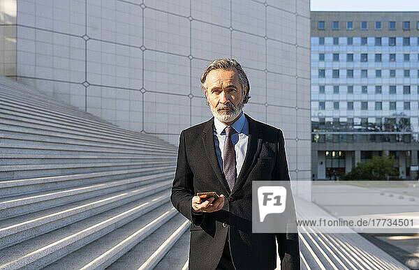 Mature businessman with smart phone standing on steps