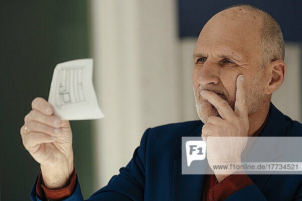 Businessman with hand on chin analyzing blueprint in office