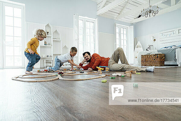 Brothers playing with toy train set by father lying at home