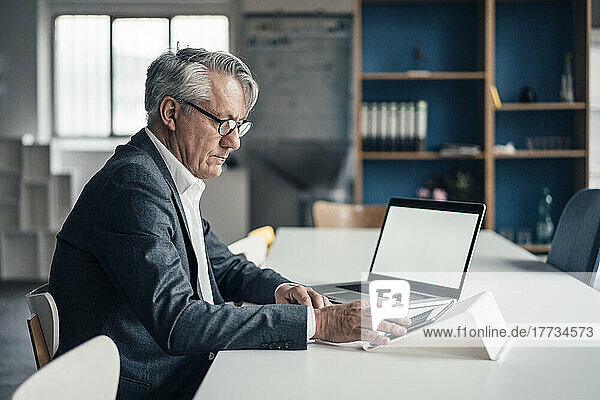 Businessman using tablet PC by laptop on desk at office
