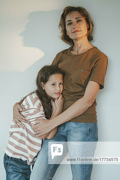 Smiling woman with daughter standing in front of wall