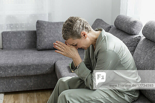 Mature woman sitting on couch in living room with hands folded