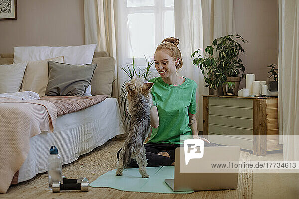 Smiling woman stroking pet dog on exercise mat at home