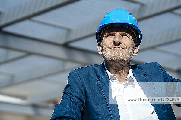 Smiling businessman wearing hardhat at construction site