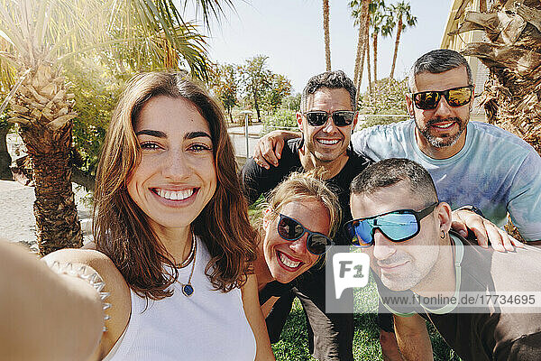 Smiling young woman taking selfie with friends on sunny day