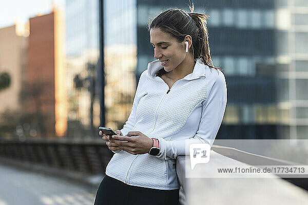 Smiling woman using smart phone leaning on railing