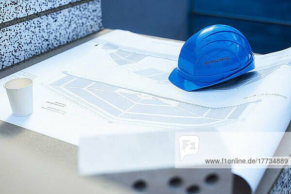 Blue hardhat and disposable cup on blueprint at construction site