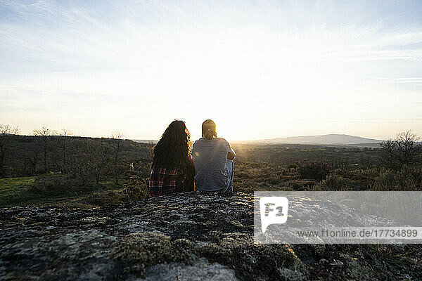 Young couple sitting on rocks admiring sunset