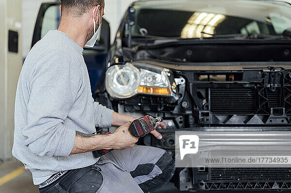 Auto mechanic repairing car with electric screwdriver in workshop