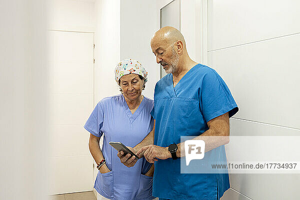 Dentist showing mobile phone to nurse standing in corridor
