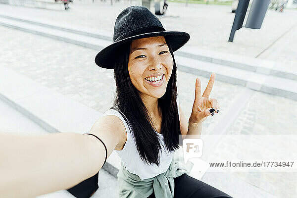 Happy woman wearing hat gesturing peace sign