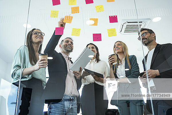 Happy business people discussing over adhesive notes in meeting at office