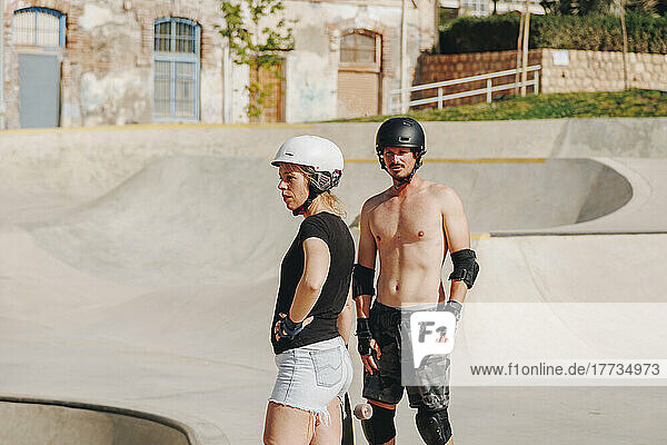 Woman with shirtless friend standing at skateboard park on sunny day
