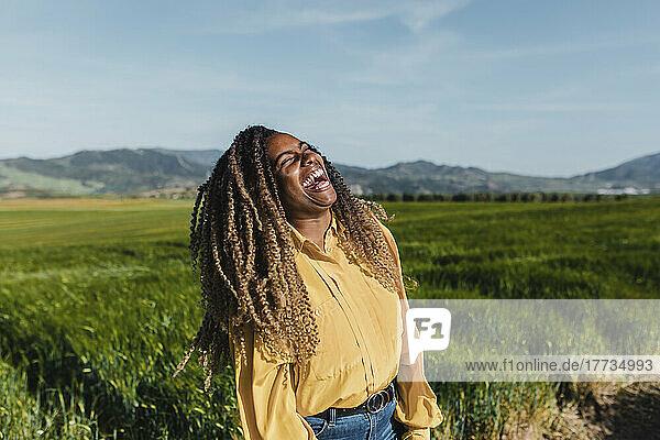 Junge Frau mit lockigem Haar lacht an einem sonnigen Tag auf der Wiese