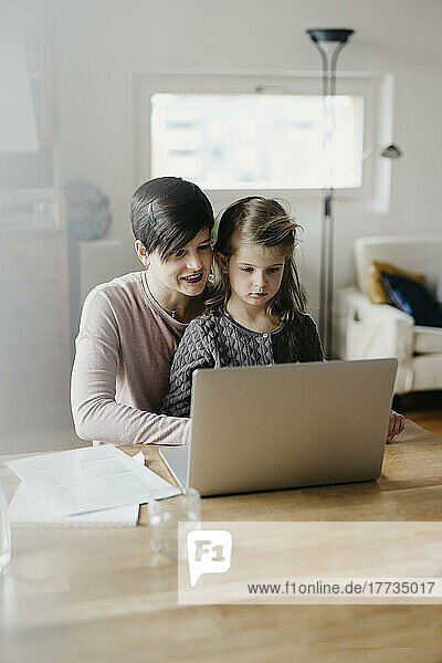 Mother and daughter watching laptop together at desk