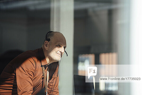Smiling businessman wearing headset in office seen through window