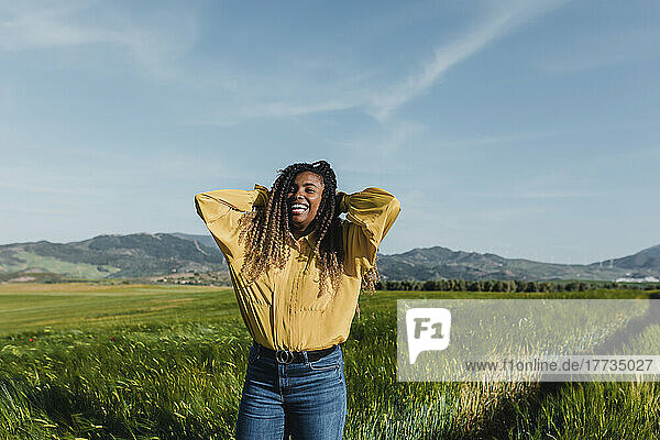 Happy woman standing with hands behind head in meadow