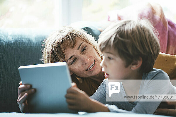 Mature woman with boy with tablet PC lying on sofa at home