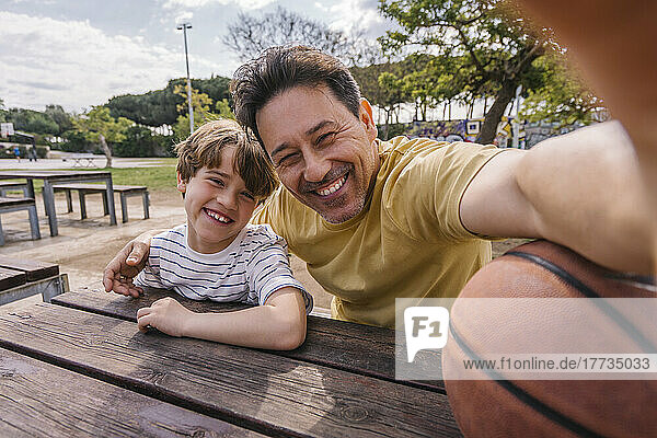 Cheerful man with son taking selfie on sunny day