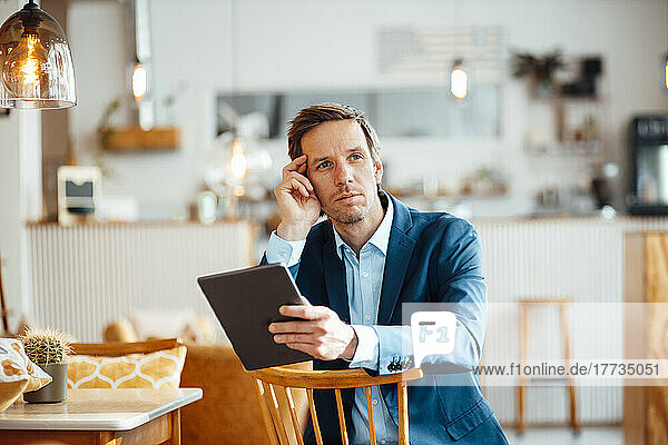 Thoughtful businessman with tablet PC sitting on chair at cafe