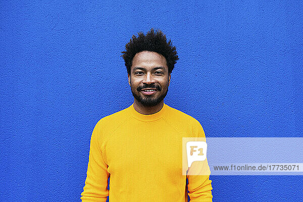 Lächelnder Afro-Mann steht vor blauer Wand