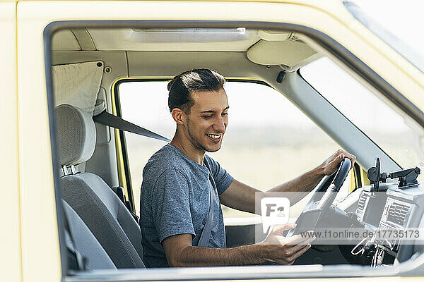 Smiling man surfing net through mobile phone sitting in van