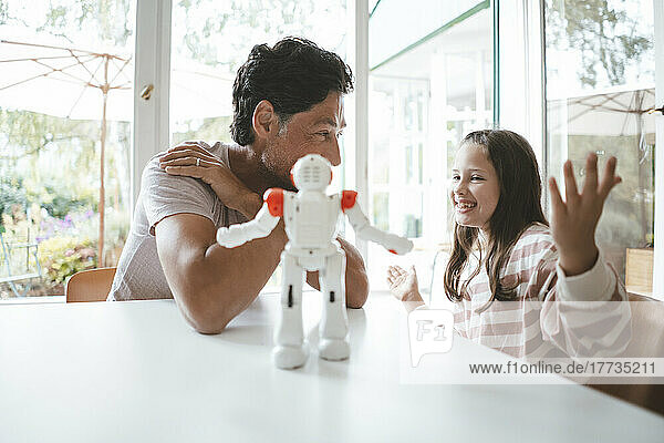 Happy daughter and father sitting with toy robot on table at home