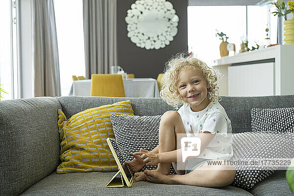 Smiling cute girl using tablet PC on couch at home