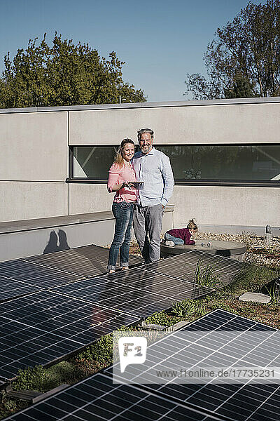 Smiling woman holding tablet PC standing with man amidst solar panel on sunny day