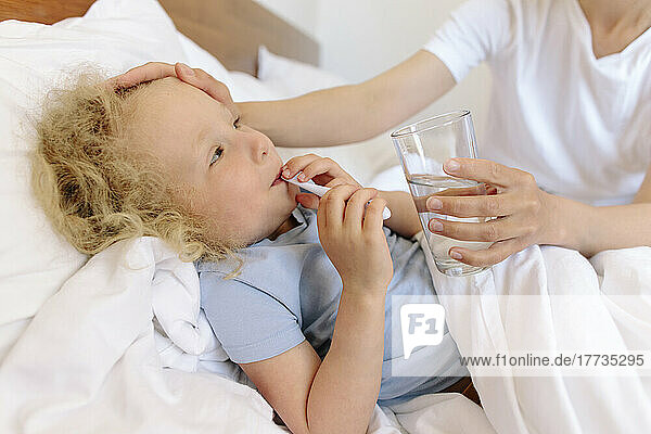 Mother giving glass of water to sick daughter lying on bed
