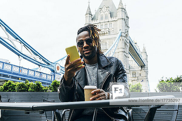 Man with sunglasses text messaging on smart phone  London  England