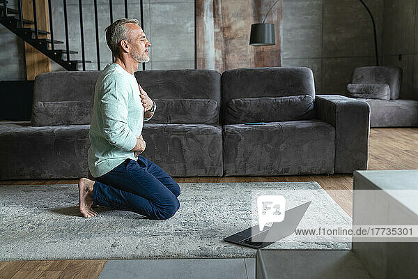 Man with eyes closed exercising on carpet in living room at home